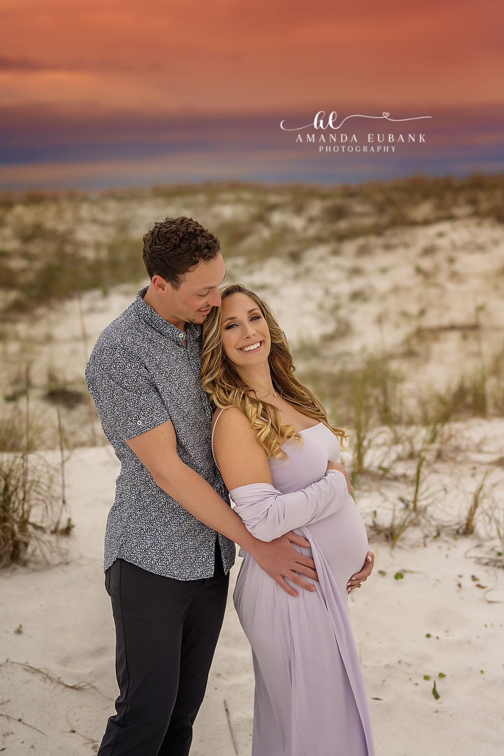 Santa Rosa Beach Maternity Photographer – Beach Dunes Couple Maternity Portrait Close-up of an expecting couple cheek to cheek among the beach dunes at dusk, the woman smiling as the man nuzzles close, photographed by a Santa Rosa Beach maternity photographer