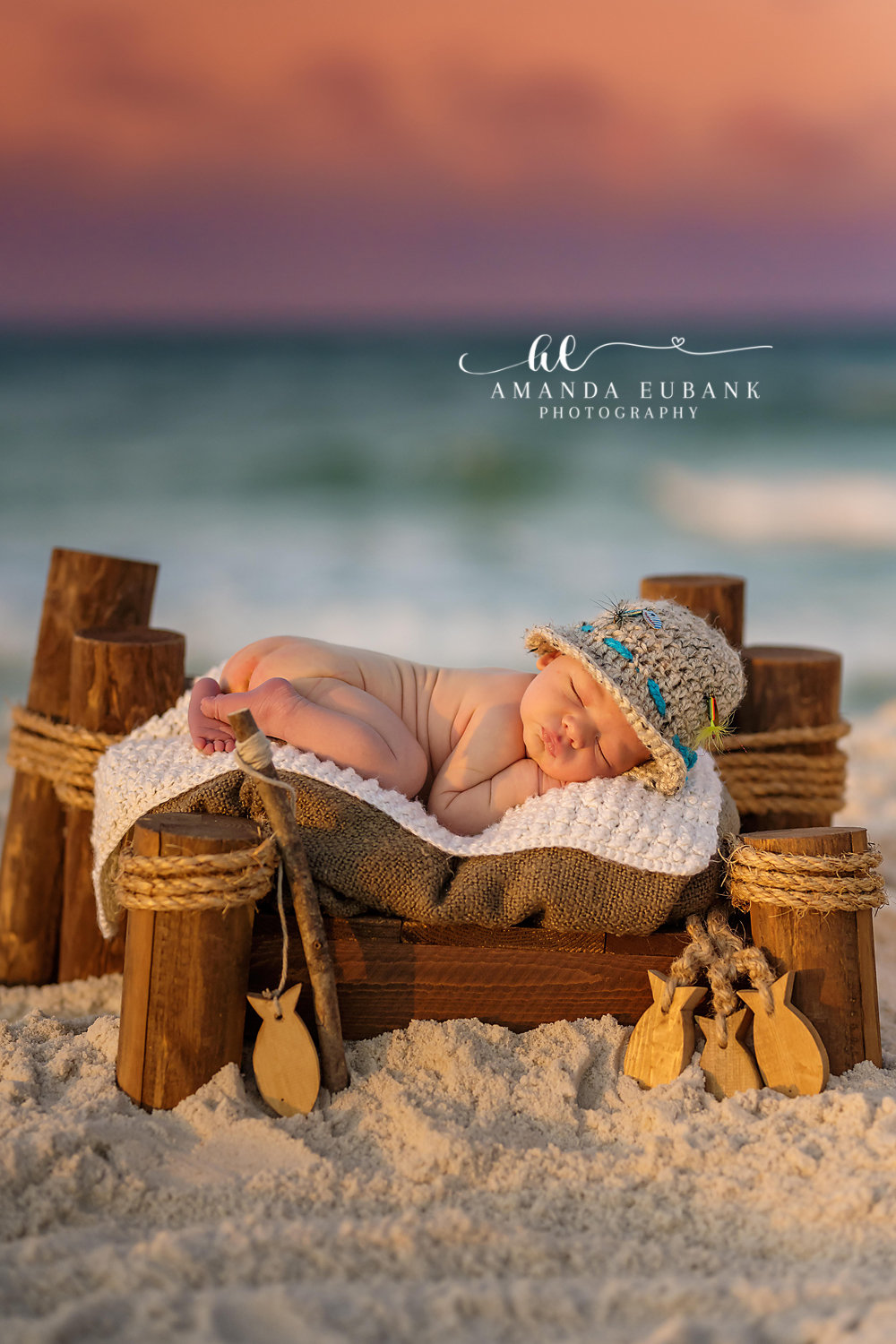 Santa Rosa Beach Newborn Photographer – Fisherman Themed Beach Newborn Session Newborn baby in a knit fisherman hat sleeping on a wooden bed with fishing props on the beach at sunset, taken by a Santa Rosa Beach newborn photographer