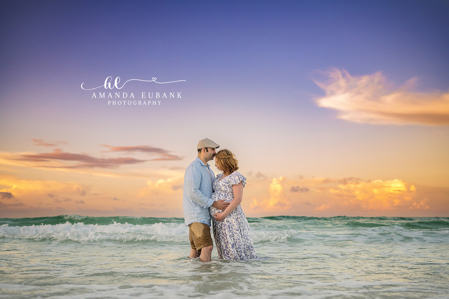 Santa Rosa Beach Photographer Maternity portrait of an expecting couple standing in the ocean waves at sunset with the woman in a floral dress, taken by a Santa Rosa Beach maternity photographer