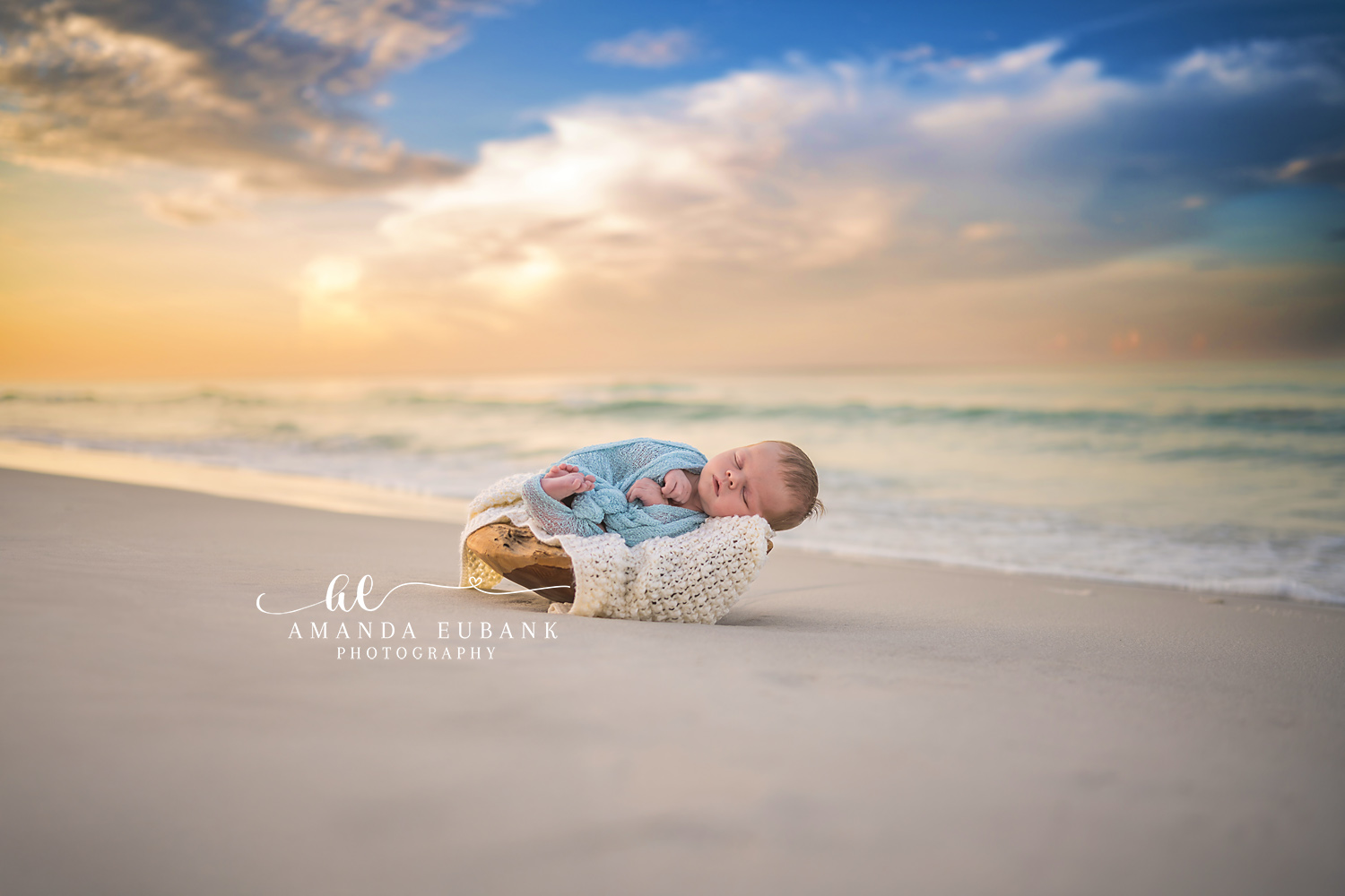 Newborn baby in a light blue wrap sleeping in a wooden bowl on the beach at sunrise, taken by a Santa Rosa Beach newborn photographer