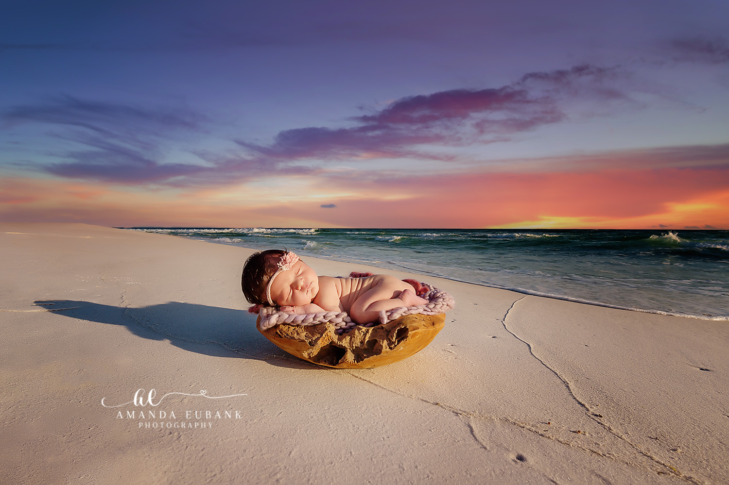 Newborn baby sleeping in a wooden bowl on the beach under a dramatic colorful sunset sky, taken by a Santa Rosa Beach newborn photographer