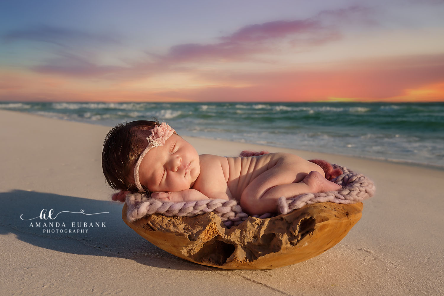 Newborn baby with a floral headband sleeping in a wooden bowl on the beach at sunset, taken by a Santa Rosa Beach newborn photographer