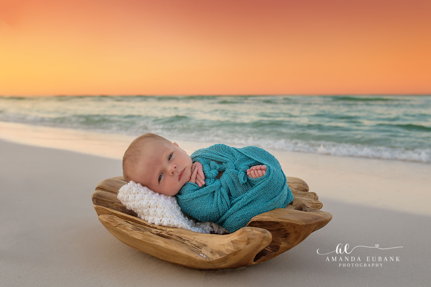 Newborn baby in a teal wrap sleeping in a wooden bowl on the beach at sunset, taken by a Santa Rosa Beach newborn photographer