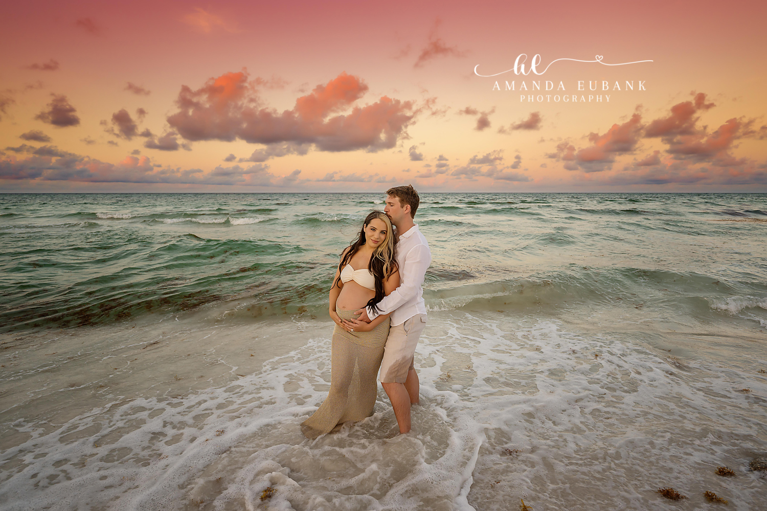 Santa Rosa Beach Photographer Maternity portrait of an expecting couple standing close together at the shoreline under a pastel sunset sky, taken by a Santa Rosa Beach maternity photographer