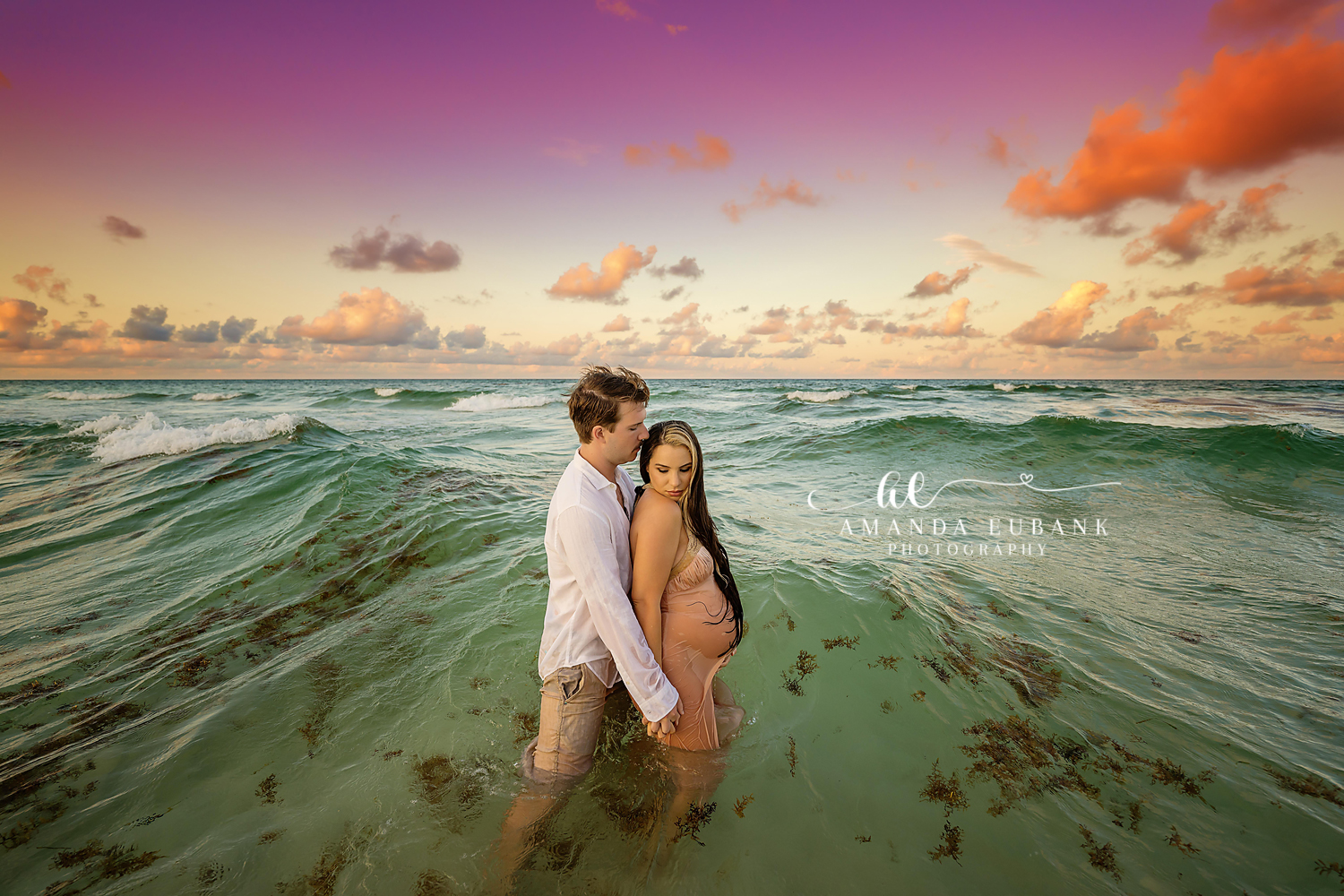 Maternity portrait of an expecting couple embracing in the ocean waves at sunset, taken by a Santa Rosa Beach maternity photographer