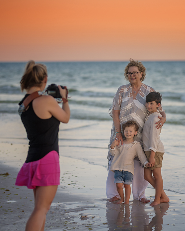 Behind-the-scenes photo of a Santa Rosa Beach photographer photographing a grandmother with her two young grandsons on the beach at sunset