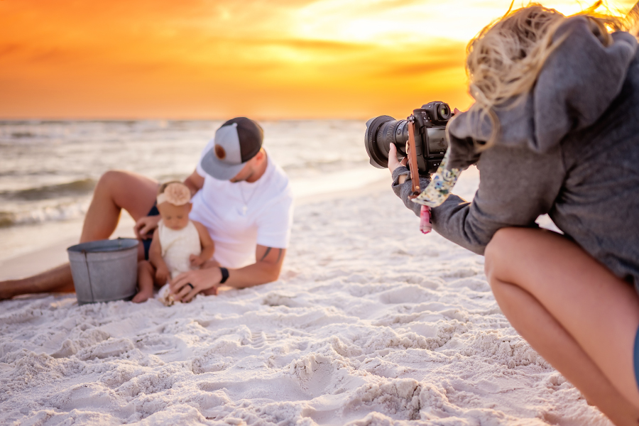 Santa Rosa Beach Photographer – Behind the Scenes Beach Family Session Behind-the-scenes photo of a Santa Rosa Beach photographer photographing a father and baby girl playing in the sand during a beach family session