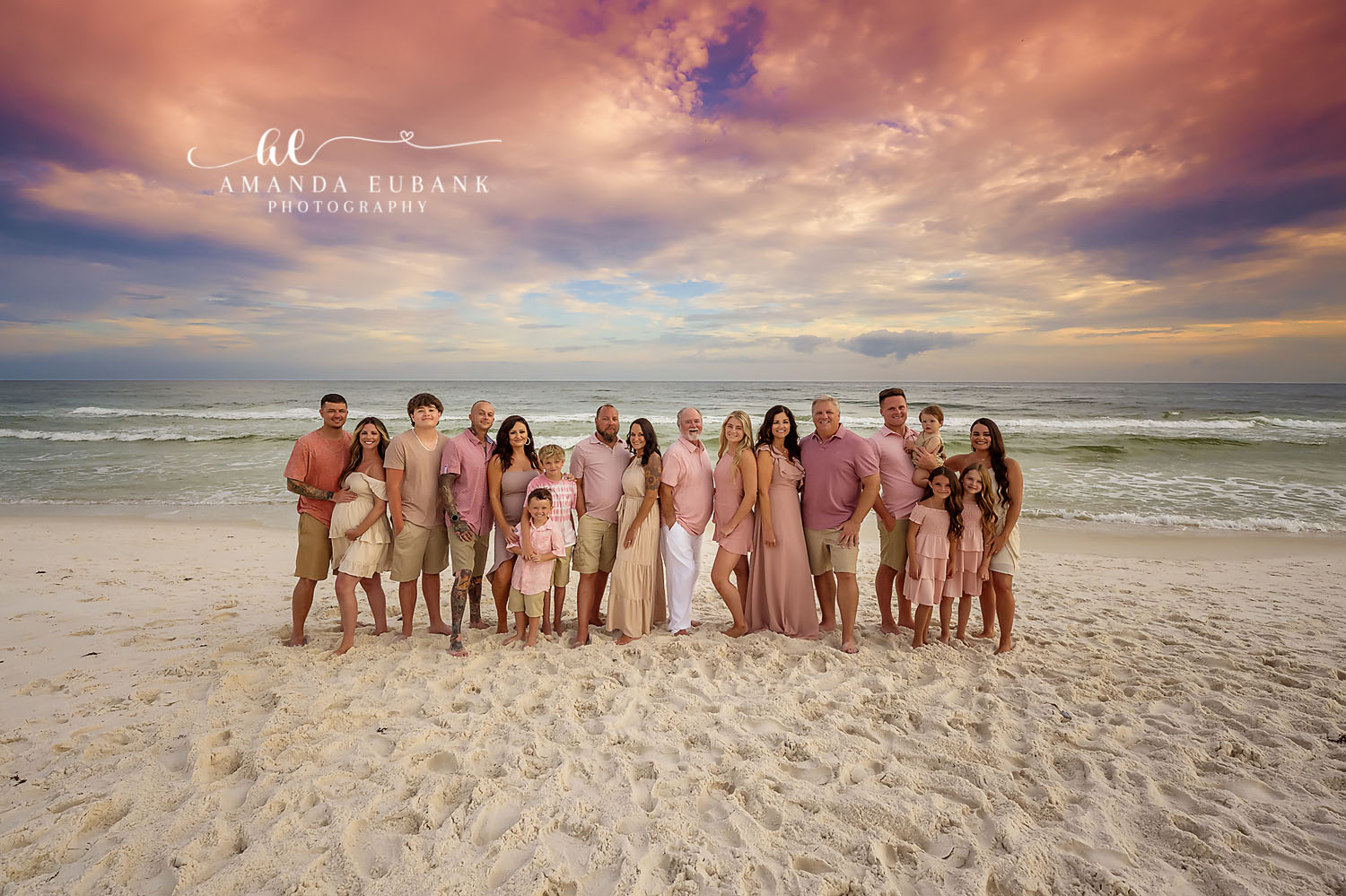 Large extended family of multiple generations posed together on the beach at sunset in coordinated pink, coral and neutral outfits, photographed by a Santa Rosa Beach family photographer