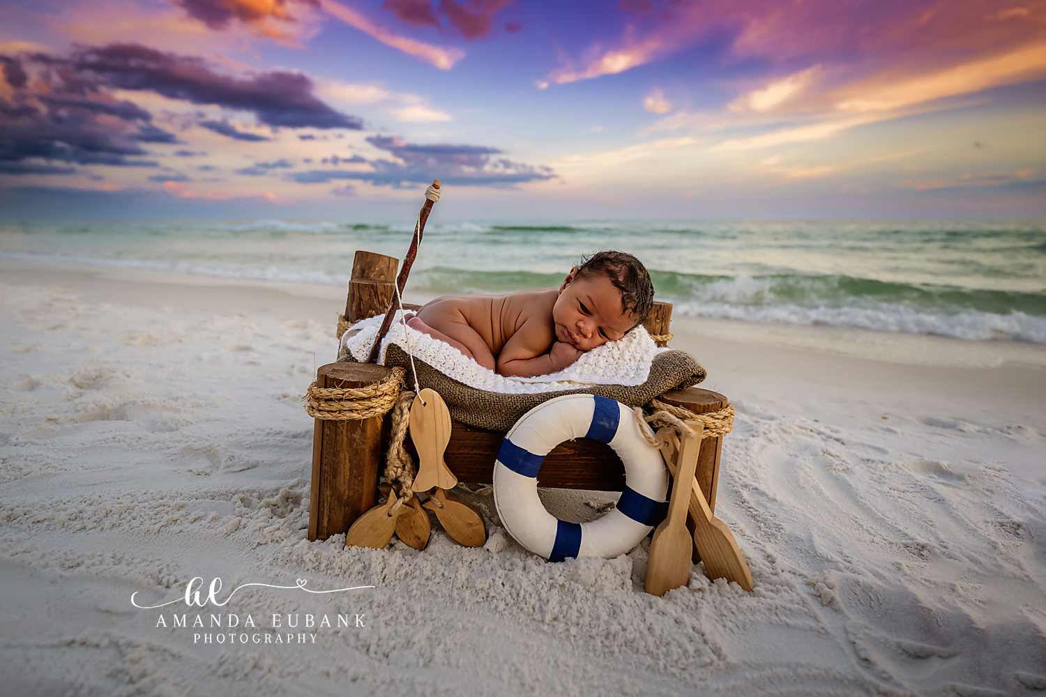 Sleeping newborn baby posed on a rustic wooden boat prop with a nautical theme of a life ring and oars on the white sand beach, photographed by a Santa Rosa Beach newborn photographer