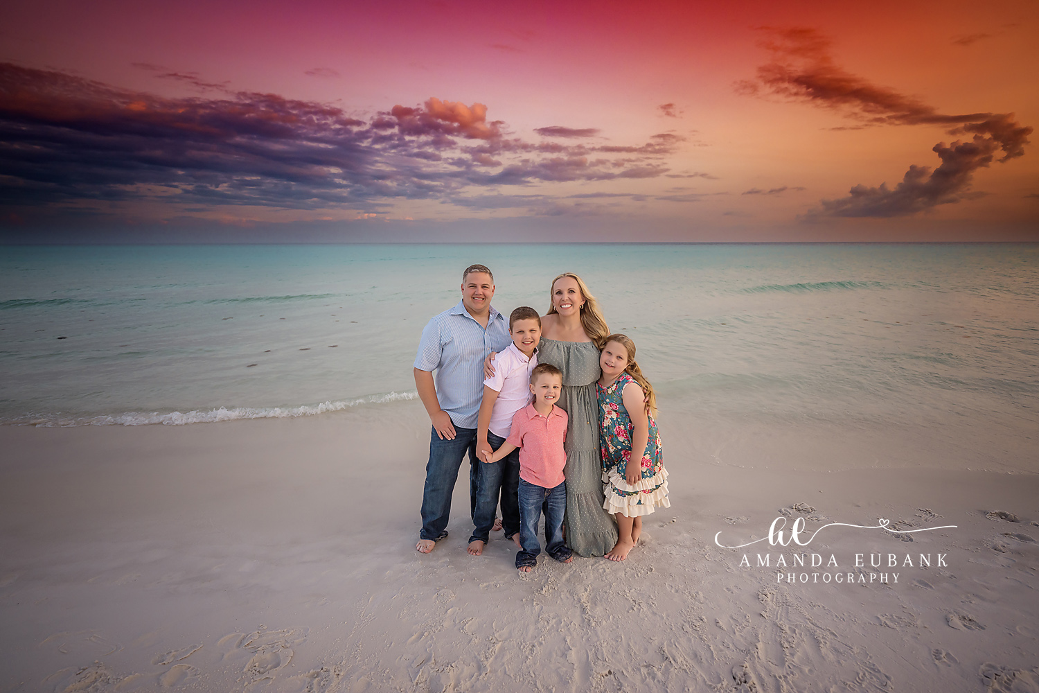Family of five in coordinated blue and neutral outfits posing together on the beach at dusk, photographed by a Santa Rosa Beach family photographer