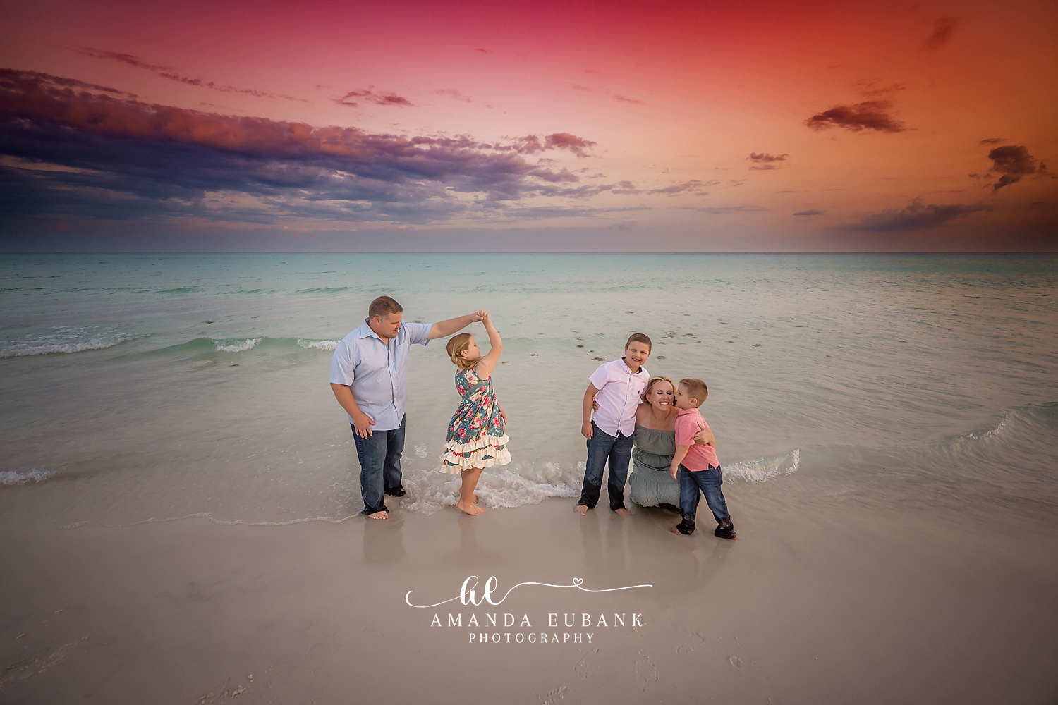 Candid family of five playing at the shoreline at dusk as the father twirls his daughter and the mother kneels with her sons, photographed by a Santa Rosa Beach family photographer