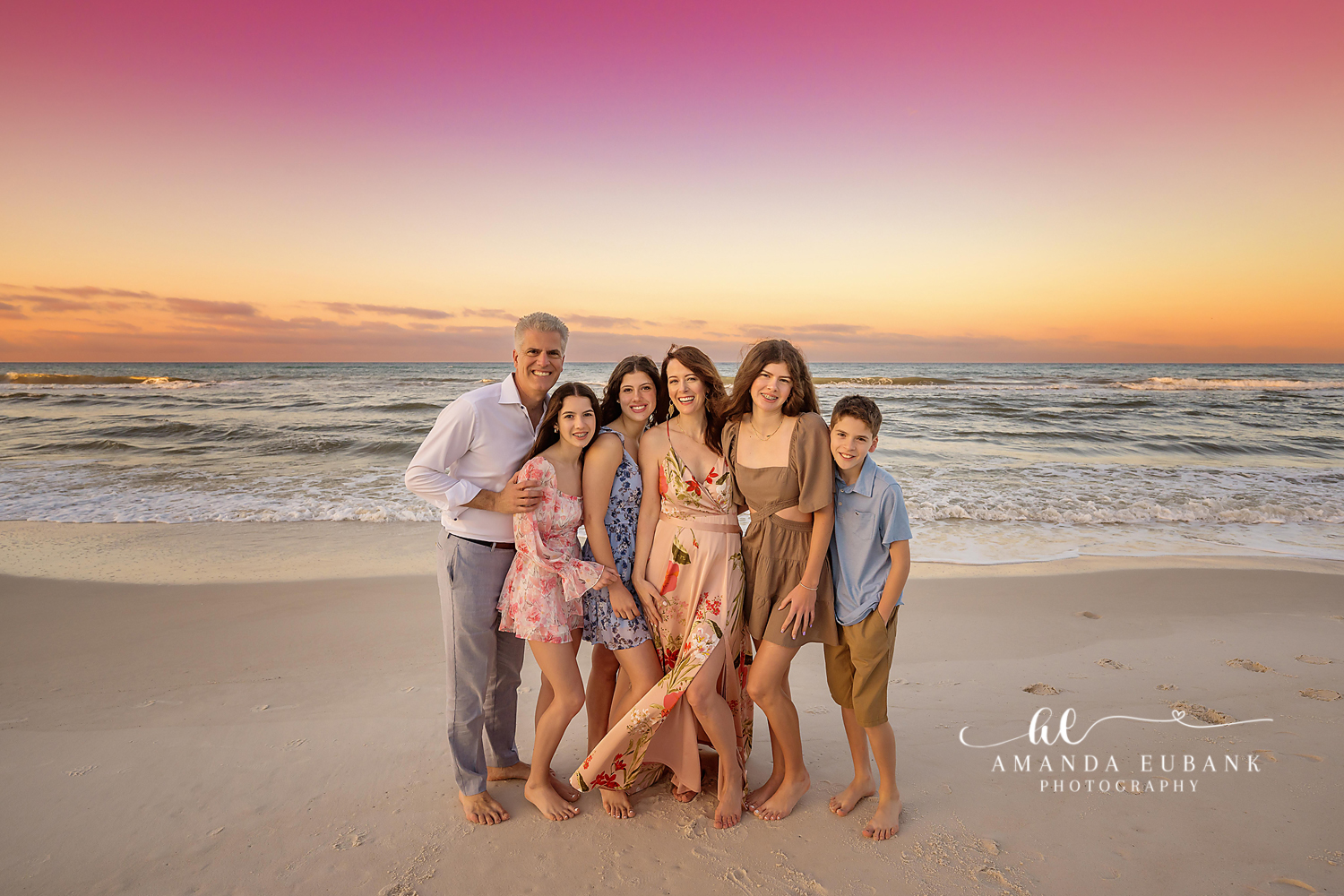 Family of six in coordinated neutral and floral outfits posing together on the beach at sunset, photographed by a Santa Rosa Beach family photographer