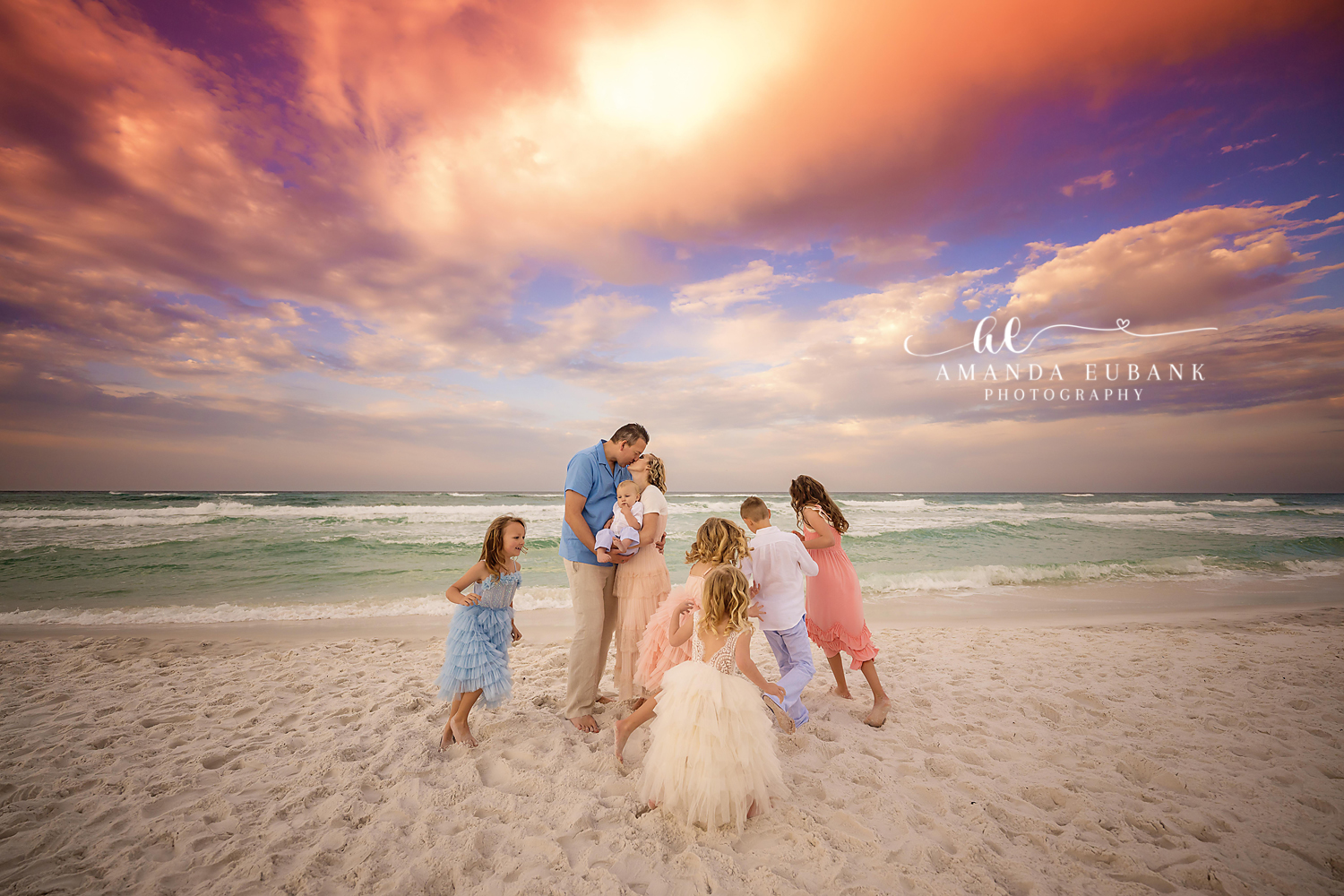 Large extended family with several children gathered together on the beach at sunset in coordinated pastel outfits, photographed by a Santa Rosa Beach family photographer