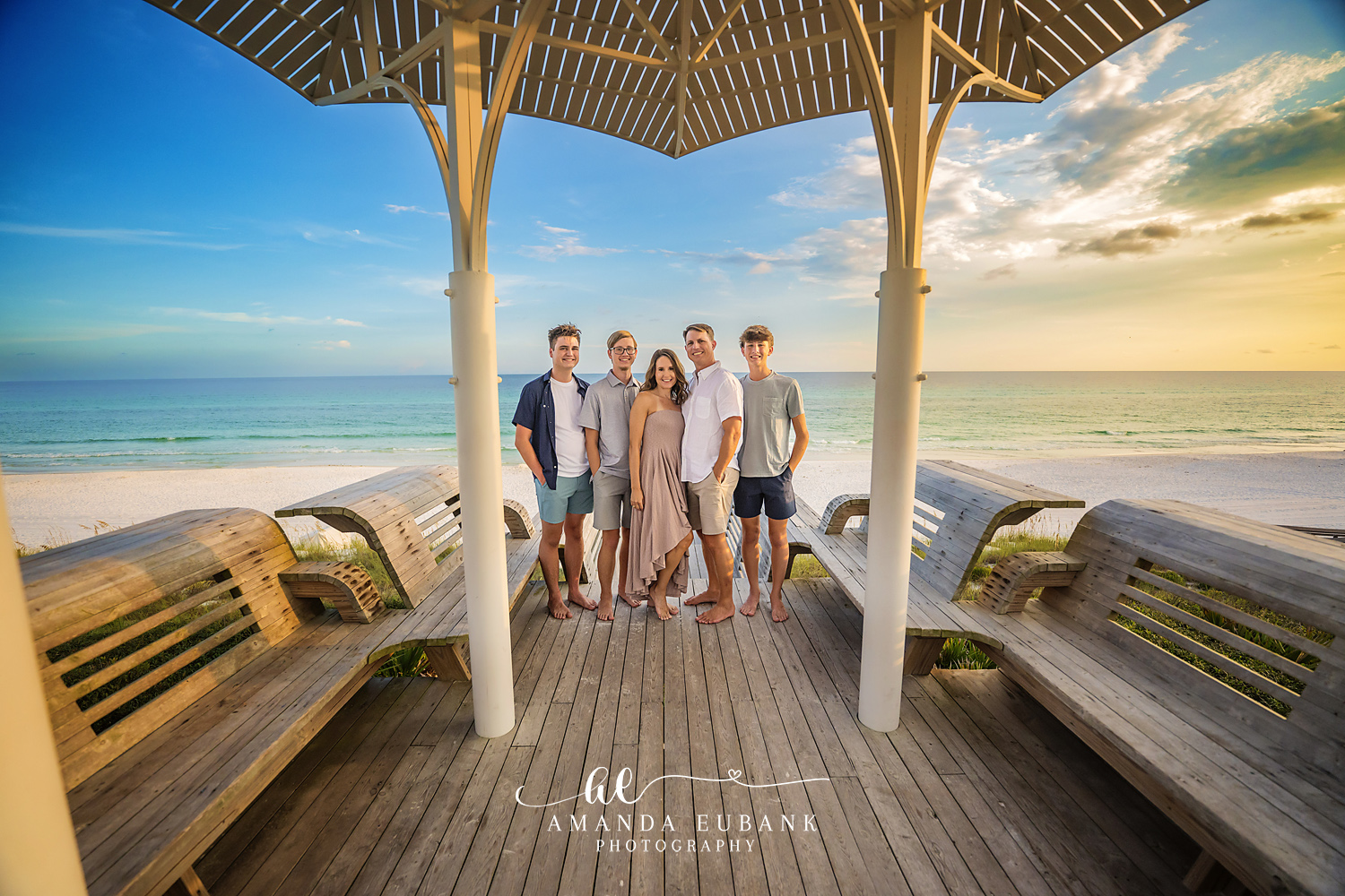 Family with grown children standing together on a beachfront pavilion deck overlooking the gulf at sunset, photographed by a Santa Rosa Beach family photographer