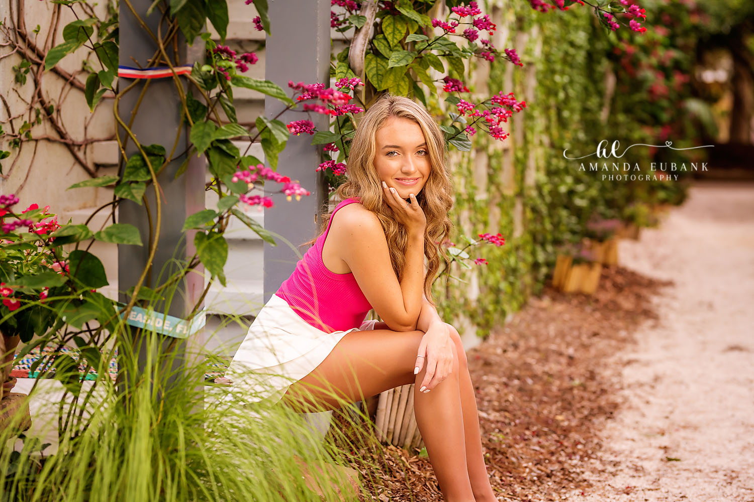 Senior girl in a hot pink top resting her chin on her hand among lush greenery and pink bougainvillea blooms, photographed by a Santa Rosa Beach senior photographer