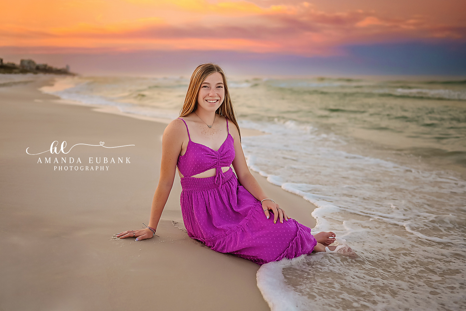 Senior girl in a magenta cutout maxi dress sitting on the wet sand at the water’s edge as the surf rolls in, photographed by a Santa Rosa Beach senior photographer