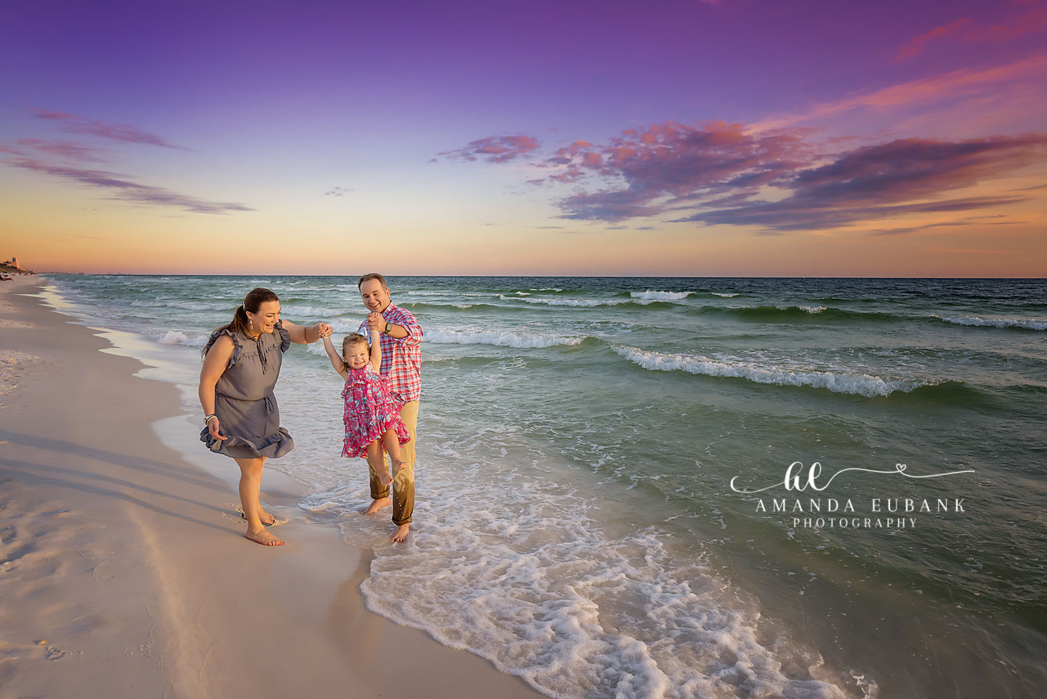 Family of three walking at the shoreline at sunset, the parents swinging their young daughter between them, photographed by a Santa Rosa Beach family photographer
