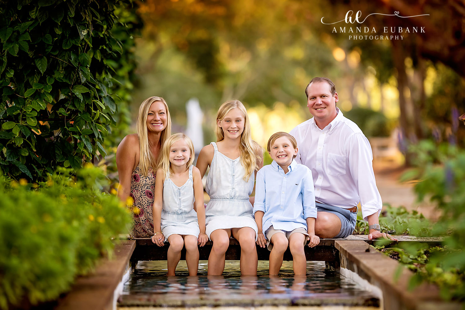 Family of five seated along the edge of a garden fountain with their feet in the water at golden hour, photographed by a Santa Rosa Beach family photographer