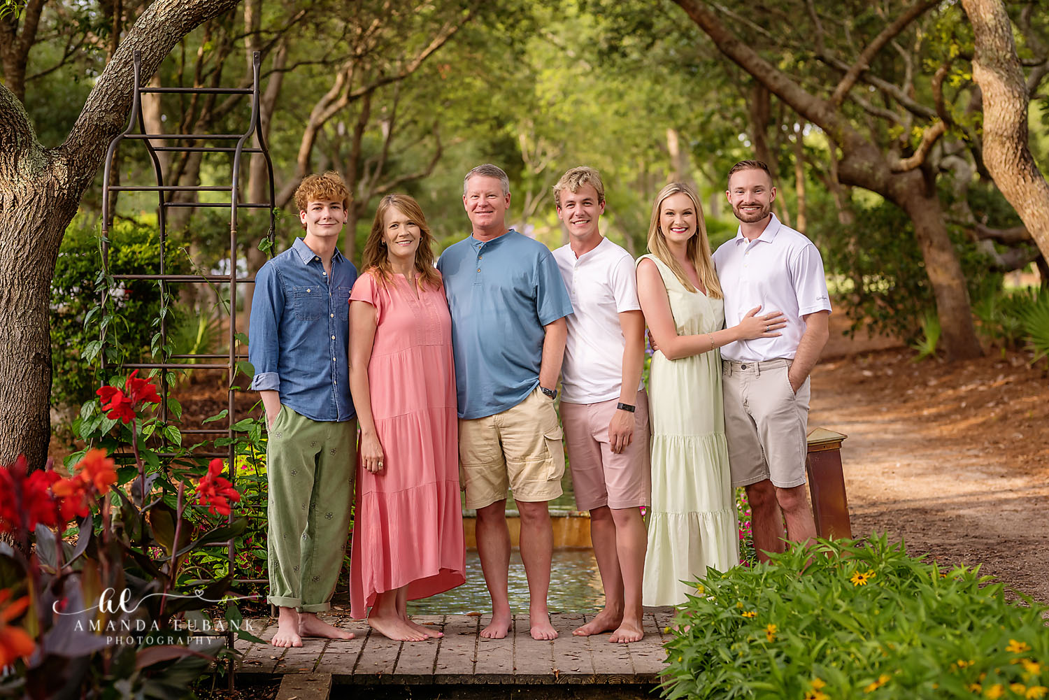 Extended family of six in coordinated outfits posed together in a lush garden setting at golden hour, photographed by a Santa Rosa Beach family photographer