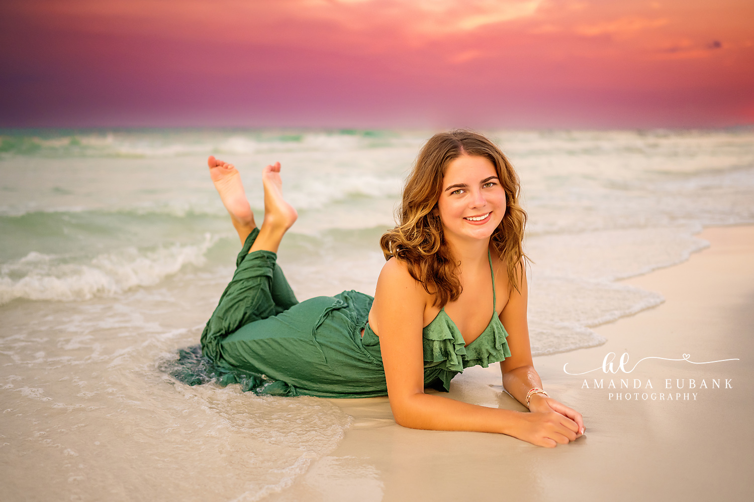 Senior girl in a green dress lying on the wet sand propped on her elbows at the shoreline, photographed by a Santa Rosa Beach senior photographer