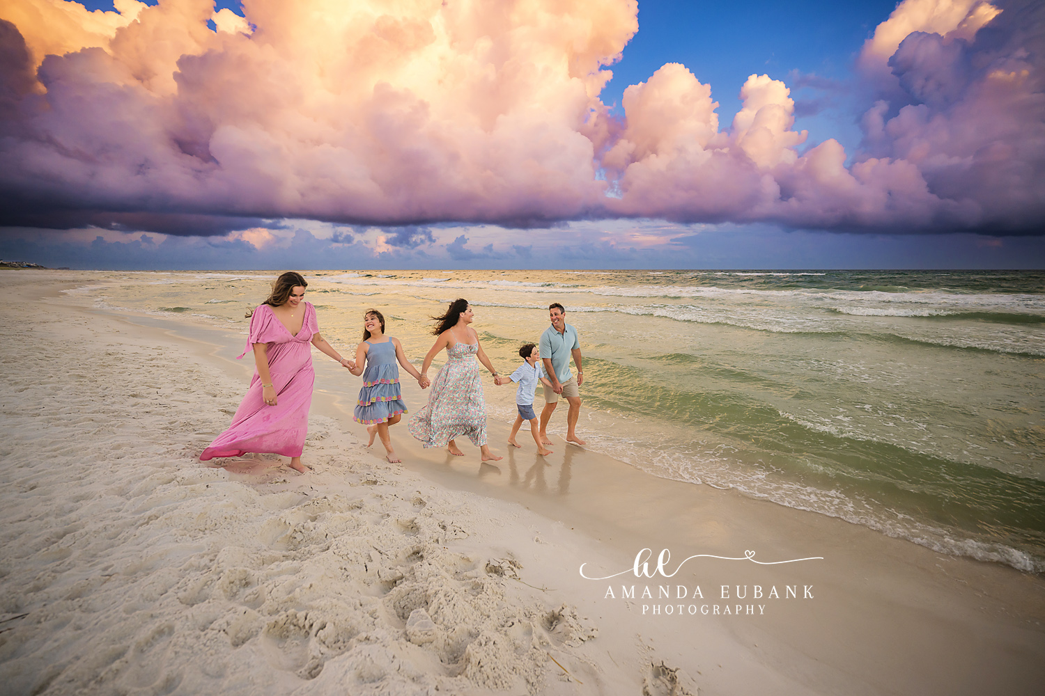 Family of five walking hand in hand along the shoreline at dusk in coordinated pastel outfits, photographed by a Santa Rosa Beach family photographer
