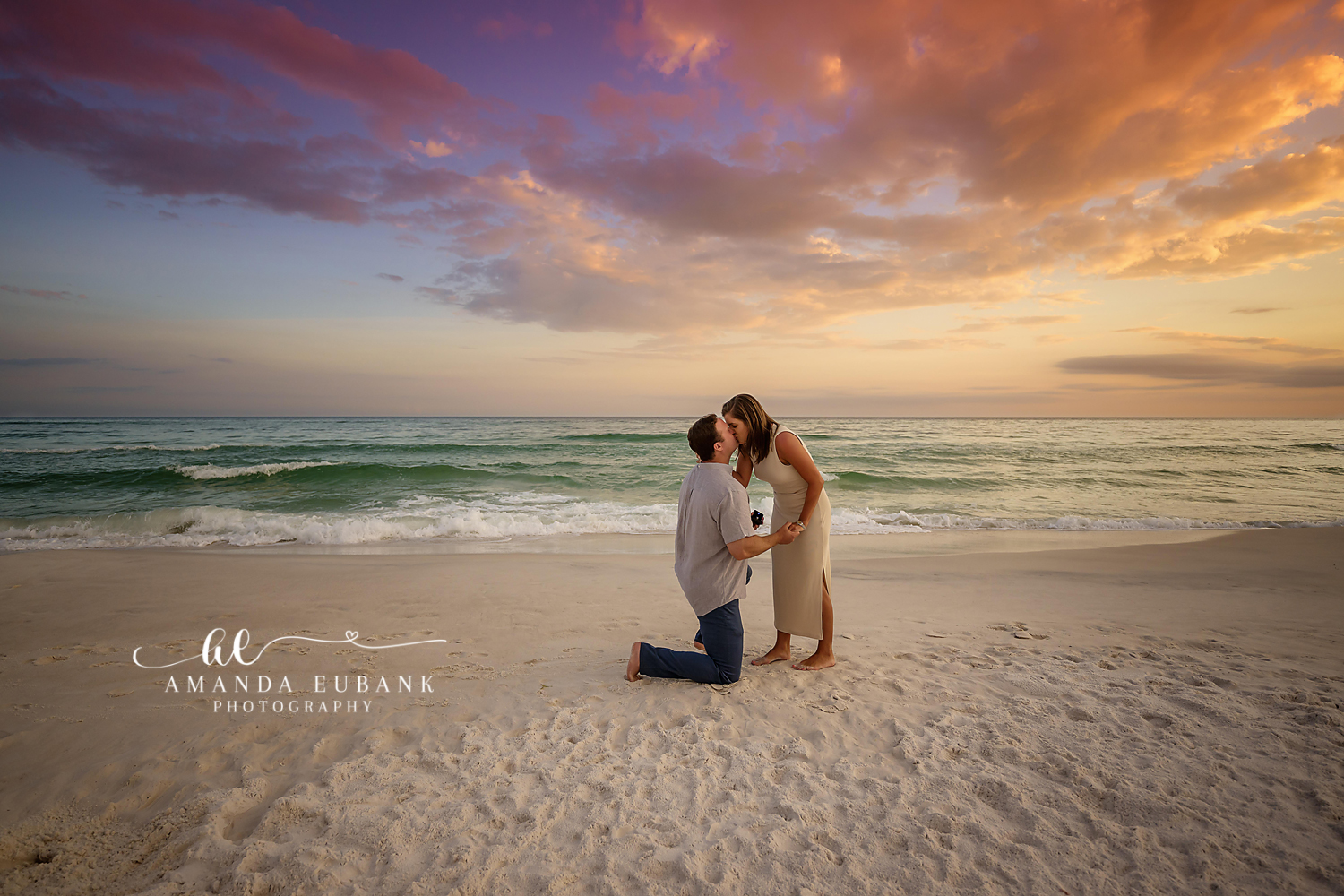 Santa Rosa Beach Maternity Photographer – Kneeling to Kiss the Baby Bump at Sunset Expecting man kneeling on the beach to kiss the baby bump of a pregnant woman in a tan dress at sunset, photographed by a Santa Rosa Beach maternity photographer