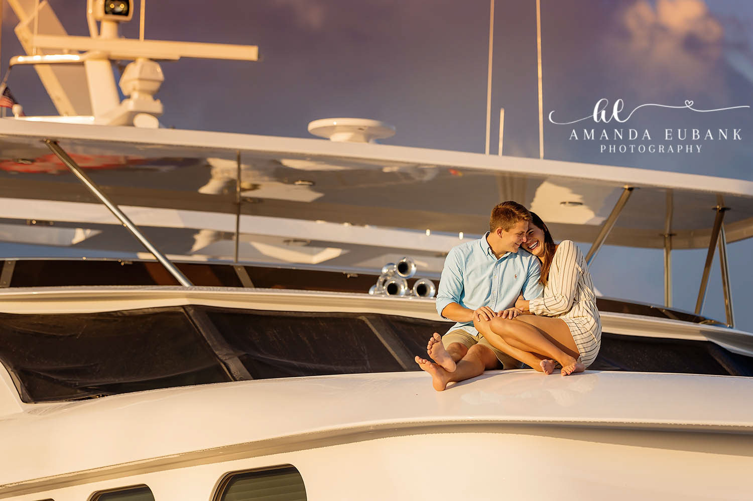 Couple cuddled together and laughing on the bow of a yacht at sunset, photographed by a Santa Rosa Beach engagement photographer