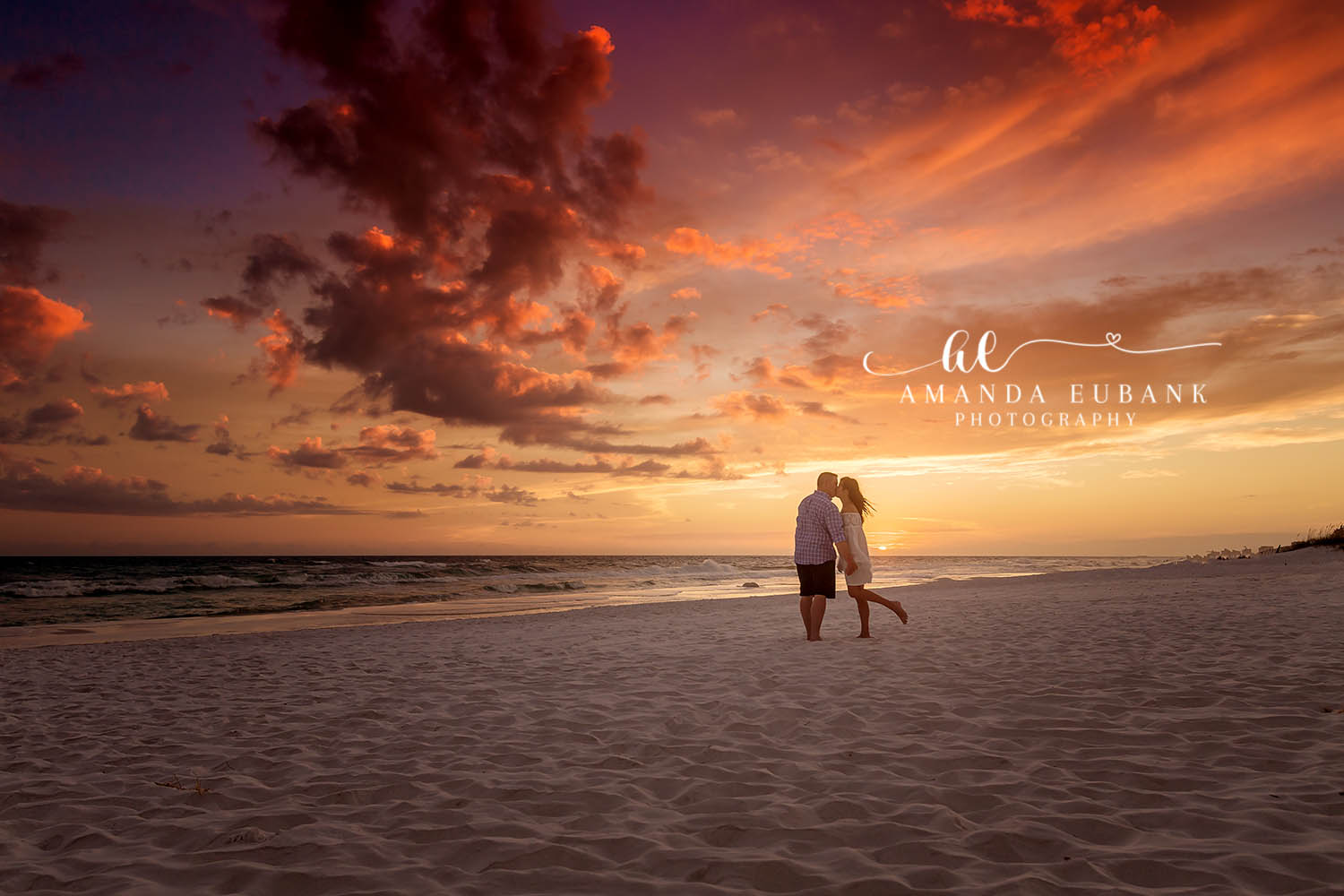 Couple standing close on the shoreline against a dramatic golden sunset sky over the ocean, photographed by a Santa Rosa Beach engagement photographer