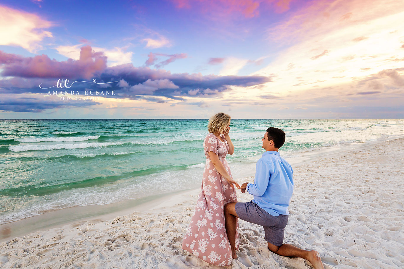 Man down on one knee proposing to a surprised woman in a pink dress on the beach at sunset, photographed by a Santa Rosa Beach engagement photographer