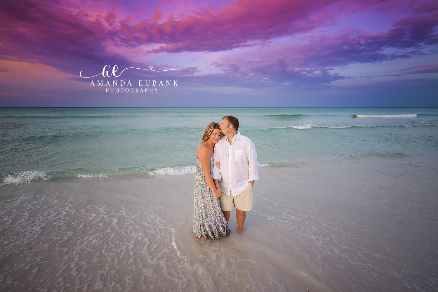 Couple cuddled close in the shallow surf at dusk as the woman rests against the man, photographed by a Santa Rosa Beach engagement photographer