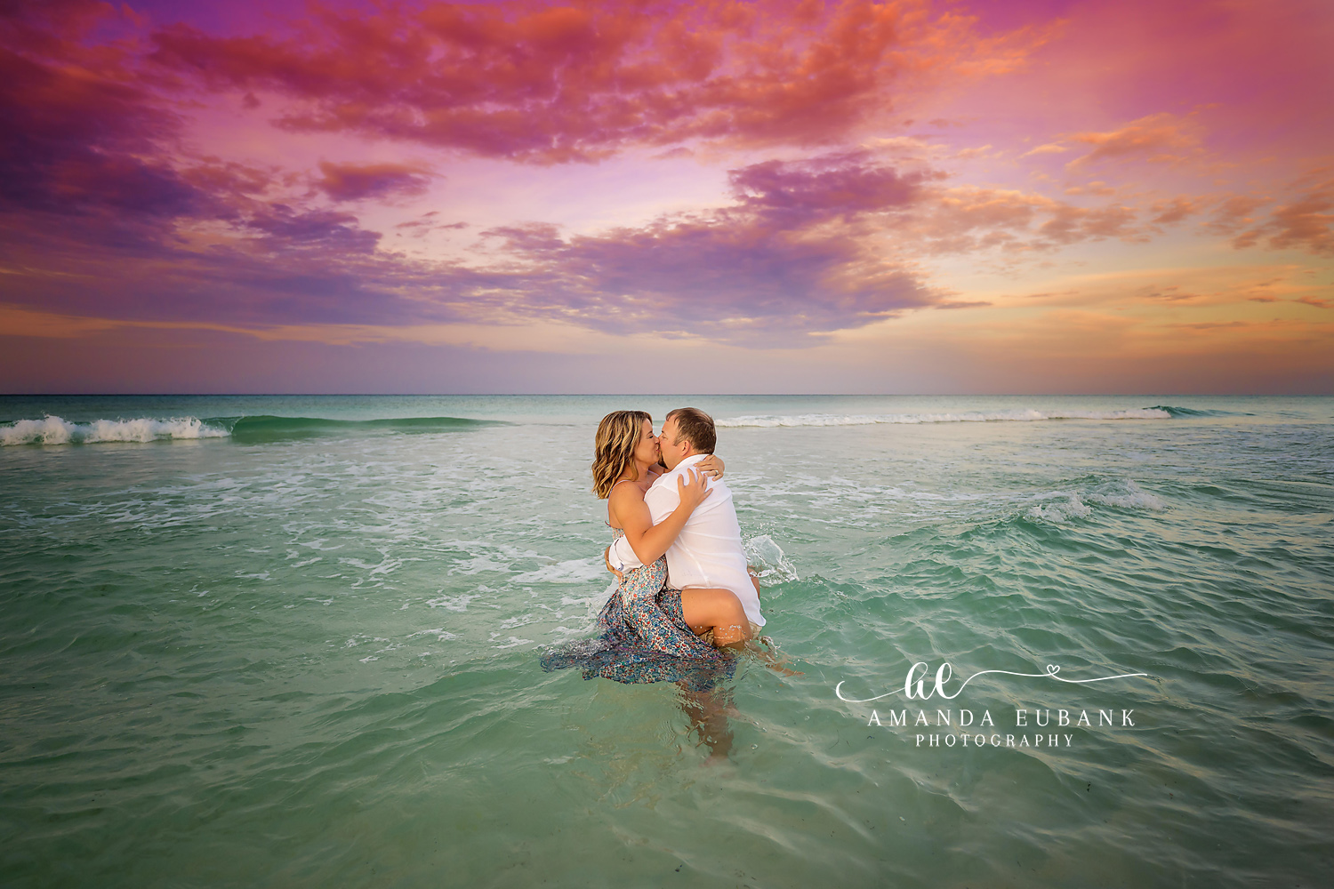 Couple kissing and embracing in the waist-deep ocean water at sunset, photographed by a Santa Rosa Beach engagement photographer